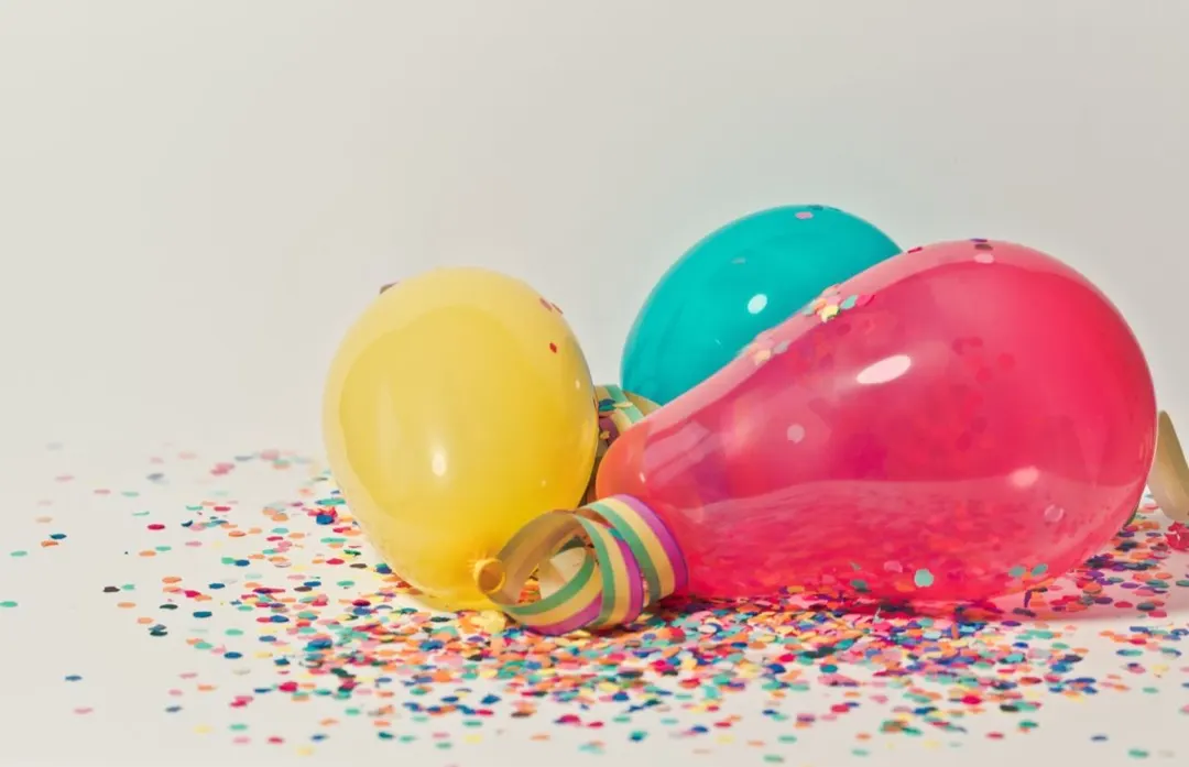 Globos amarillos, azules y rojos sobre una mesa con confeti