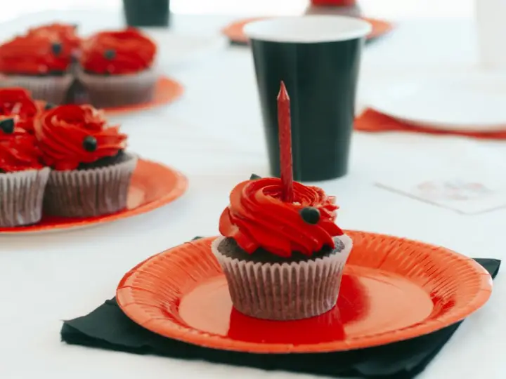 Platos desechables rojos servidos con cupcakes en una mesa de fiesta
